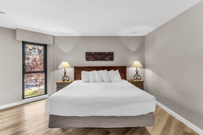 A hotel room with a large bed, two bedside tables with lamps, a window with a view, and a decorative wall piece.