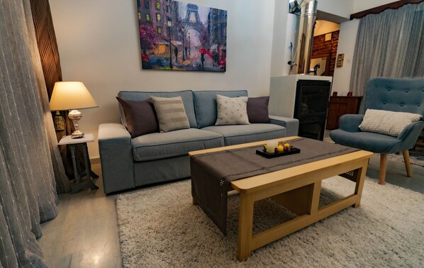 A living room with a grey sofa, a wooden coffee table, a blue armchair, a painting of a cityscape, and a lamp.