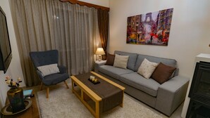Een woonkamer met een grijze bank, een blauwe fauteuil, een houten salontafel en een schilderij van een stadsgezicht.