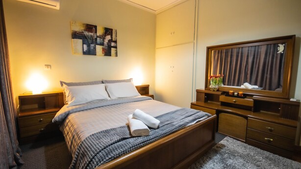 Een netjes opgemaakt bed met een grijs-witte gestreepte deken, een houten hoofdbord en twee bedlampjes.
