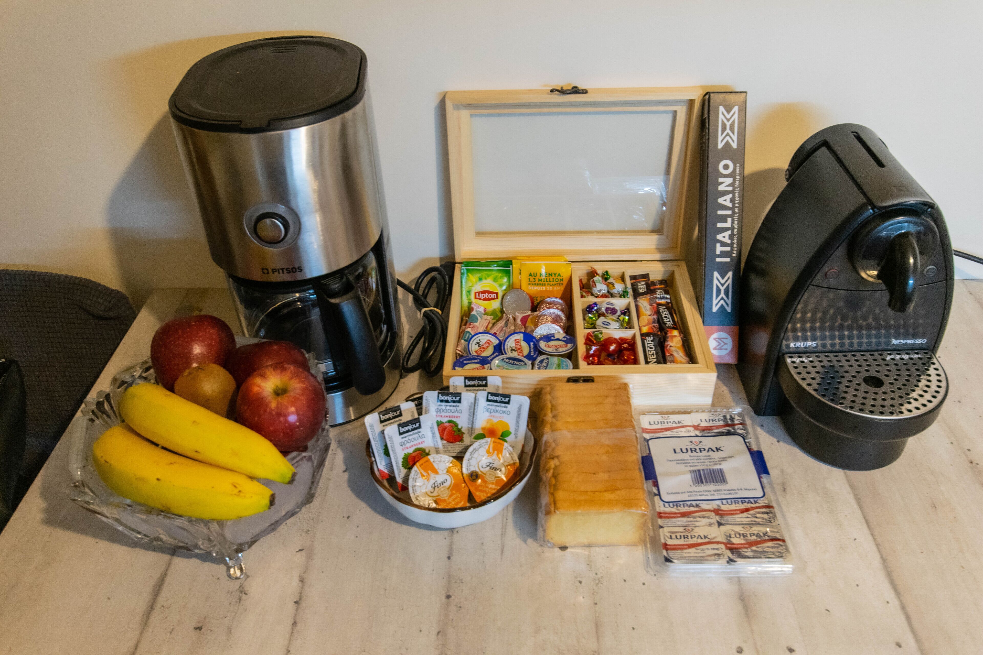 Colazione con una macchina da caffè, un quadro incorniciato, una scatola di snack italiani, una ciotola di frutta, un piatto di formaggio e una confezione di burro Lurpak.