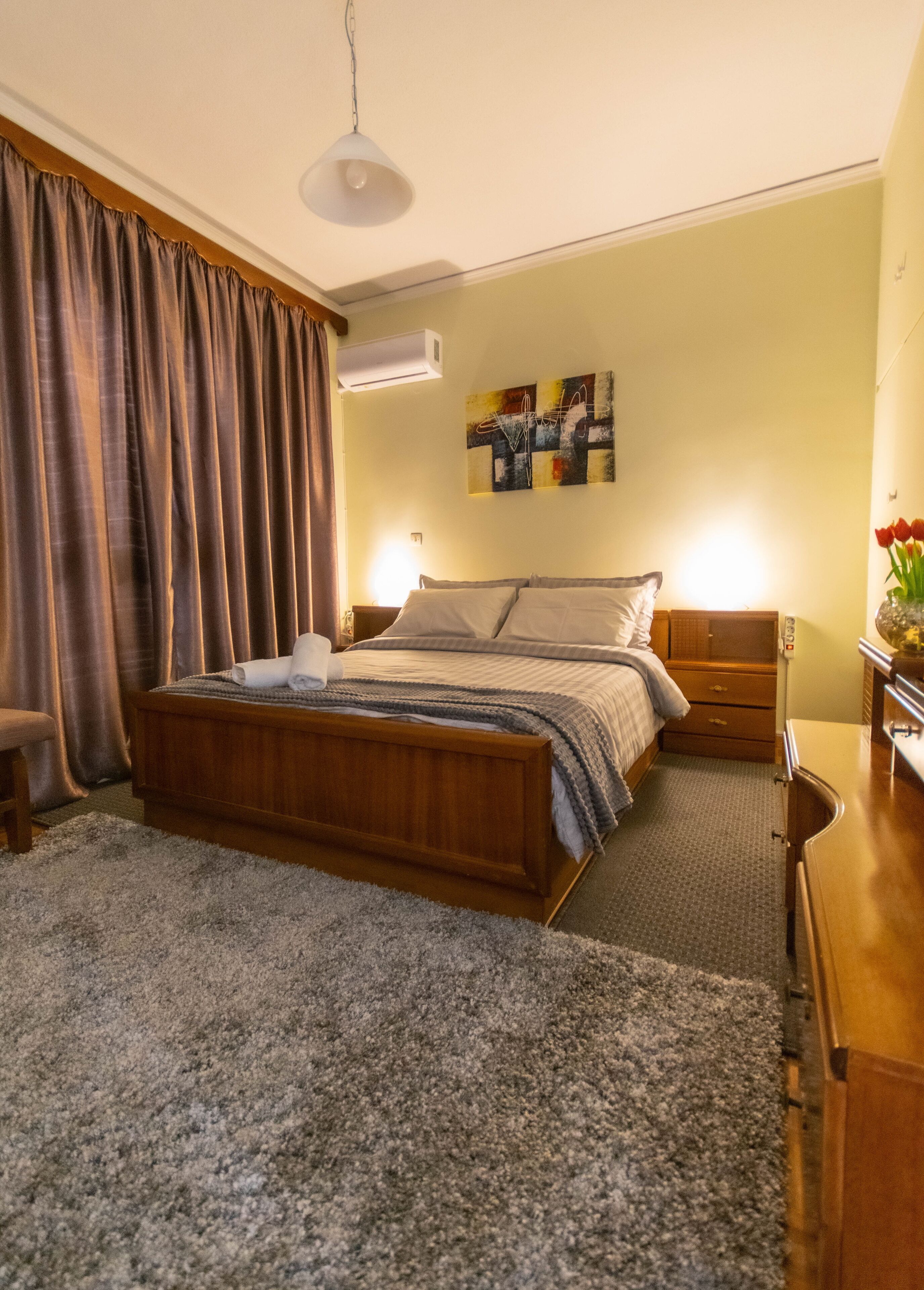 Une chambre à coucher avec un lit en bois, un bureau, une chaise, une lampe et un tableau accroché au mur.