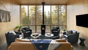 A modern living room with a large window, a fireplace, and leather furniture. - Scandinavian Chalet with Sauna in Lutsen - Blue (Lutsen)