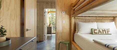 A wooden cabin interior with a bed labeled "CAMP," a small stool, and a dresser with a plant.