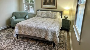 A bedroom with a large bed, a chair, a nightstand with a lamp, and a framed picture on the wall. - Bayside Tranquility - A Birder’s Paradise (Lower Township)