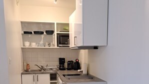 A compact kitchen with white cabinets, a microwave, a coffee maker, and a small dining table with chairs. - Studio Calme Brest Hyper Centre (Brest)
