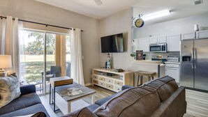 Una sala moderna con sofá, mesa de centro y televisor. Hay una zona de cocina con microondas y refrigerador.