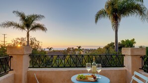 Un balcon avec une table dressée pour deux personnes, agrémentée d’une bouteille de vin, de verres et d’une assiette de fruits.
