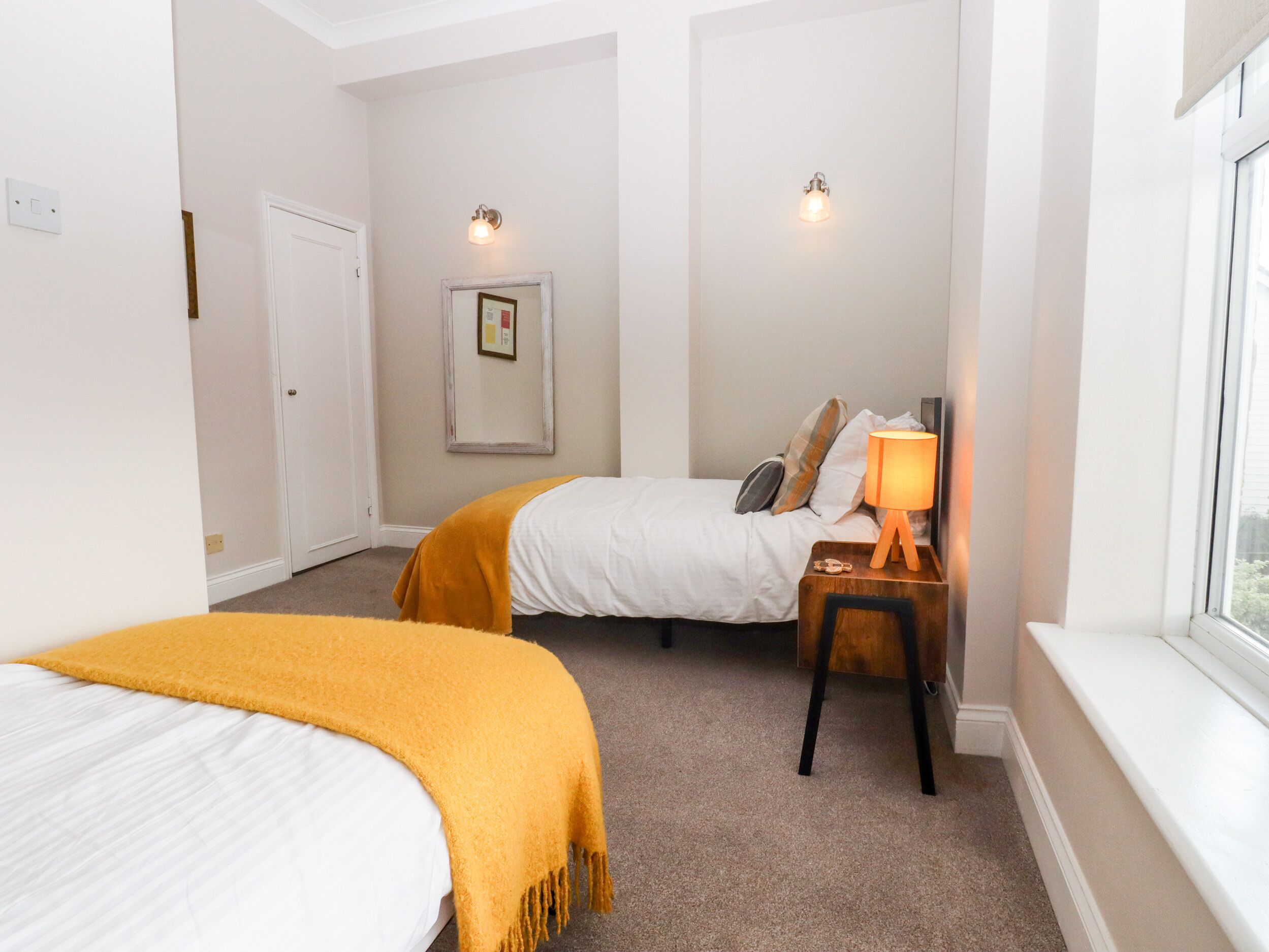Una habitación de hotel con dos camas, una ventana, una lámpara de noche y un cuadro en la pared.