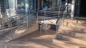 A modern interior with a glass railing staircase, a metal handrail, and a tiled floor. - Art Plaza (Tashkent)