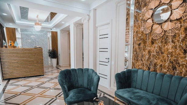 A modern lobby with a reception desk, two green upholstered sofas, a glass coffee table, and a decorative mirror on the wall. - Art Plaza (Tashkent)