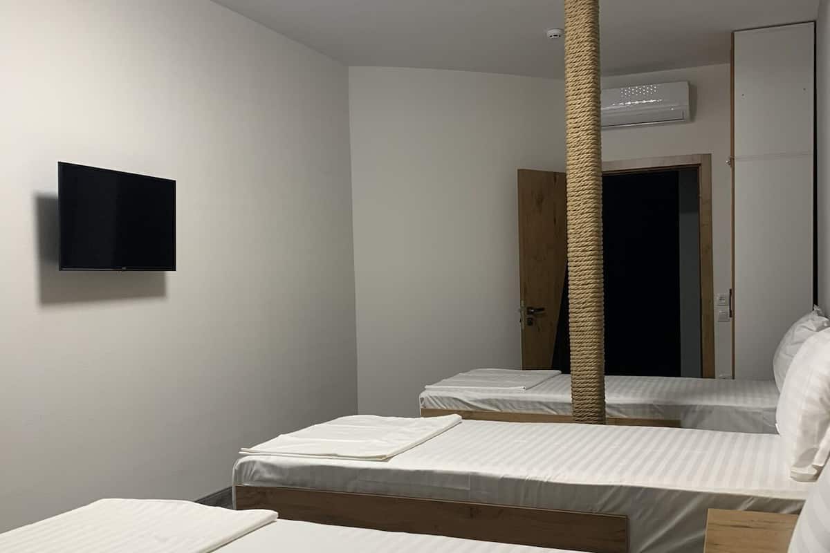 A room with three beds, a mounted TV, a ceiling light, and a wooden door.