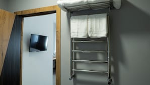 A bathroom with a towel rack holding folded towels, a flat-screen TV mounted on the wall, and a wooden door frame. - Art Plaza (Tashkent)