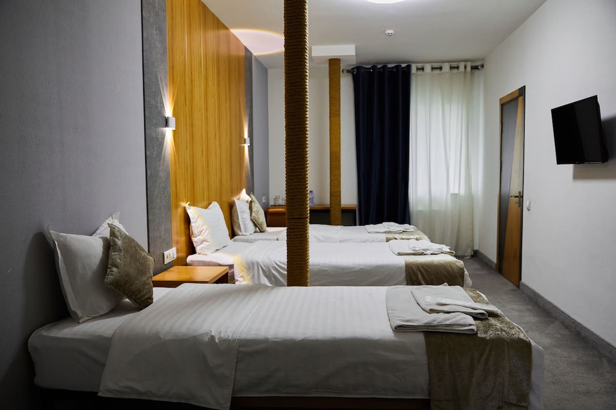 A hotel room with two beds, a wooden column, a flat-screen TV, and a window with curtains.
