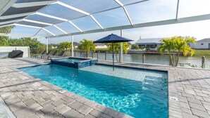 An indoor swimming pool with a clear view of the surrounding area, including a covered patio and a body of water. - Heated Pool and Spa Villa with Waterfront Views and Kayaks! (Cape Coral)
