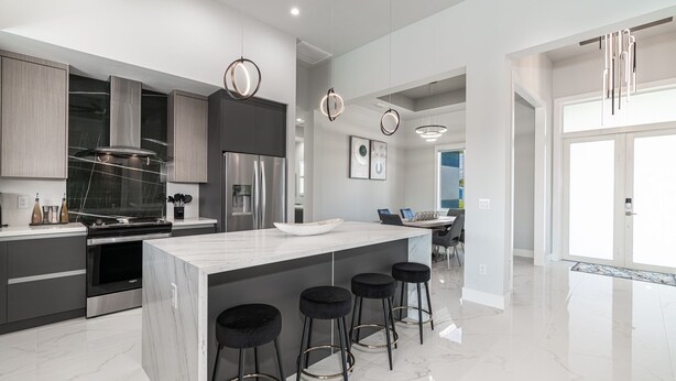 A modern kitchen with a central island, bar stools, stainless steel appliances, and pendant lighting. - Heated Pool and Spa Villa with Waterfront Views and Kayaks! (Cape Coral)