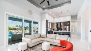 A modern living room with a sectional sofa, a red armchair, and a large glass door leading to a pool area. - Heated Pool and Spa Villa with Waterfront Views and Kayaks! (Cape Coral)