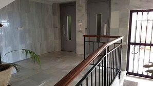Un intérieur moderne avec un sol en marbre, un escalier en bois doté d’une rampe noire et une porte avec une poignée verticale.