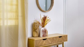 A wooden console table with a mirror above it, a vase with dried plants, and a sheer curtain partially covering a window. - Cocon Dumyse, proche du Jardin botanique (Petit-Bourg)