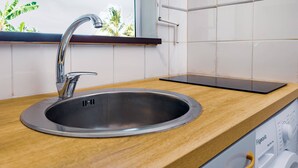A modern kitchen with a stainless steel sink, wooden countertop, and a window with a view of palm trees. - Cocon Dumyse, proche du Jardin botanique (Petit-Bourg)