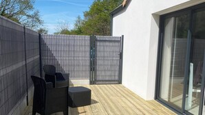 A wooden deck with a metal fence, a glass door, and outdoor furniture. - Maison à 15 Minutes de la mer (Saint-Urbain)