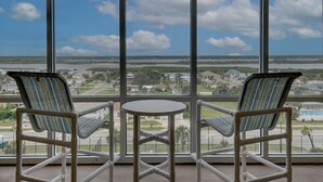 Een balkon met twee gestreepte stoelen en een kleine tafel, met uitzicht op de kustlijn, huizen en water.