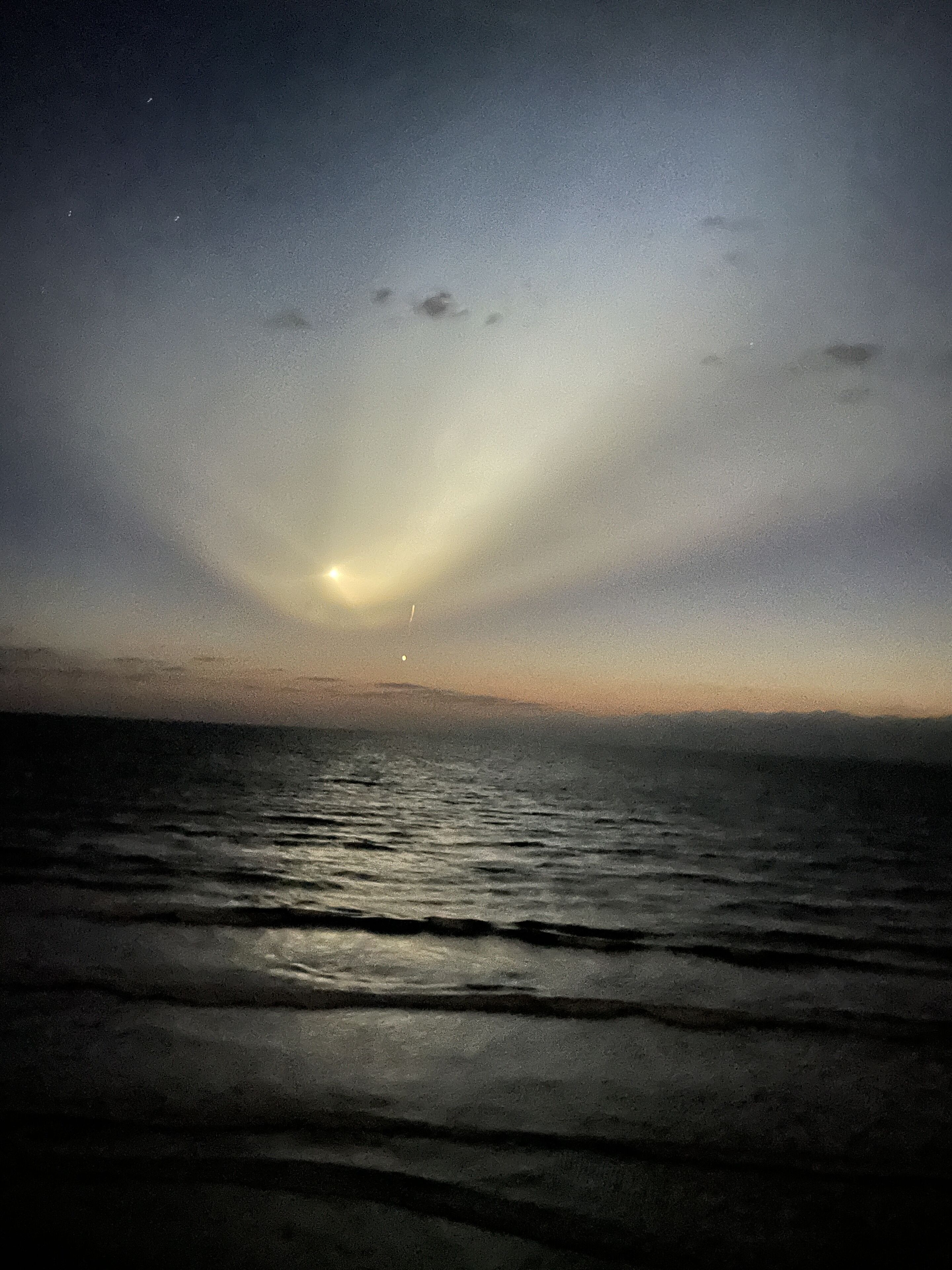 Ein Strandbild bei Nacht mit Wellen und Mond am Himmel.