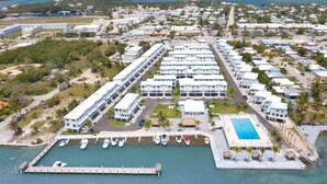 Un resort con varias edificaciones blancas, un muelle con barcos y una piscina.