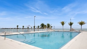 Una piscina rectangular con superficie de agua azul cristalina, rodeada por una terraza blanca y palmeras.