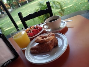 Un desayuno con un plato de pasteles, un vaso de zumo de naranja y una taza de café sobre una mesa con vistas a un jardín.