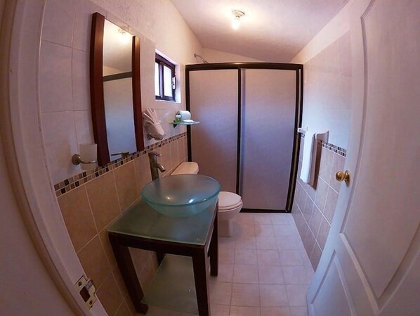Un baño con lavamanos de vidrio, inodoro y zona de ducha.