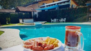 A poolside table with a plate of food and a glass of beverage, surrounded by a pool and outdoor seating. - Hotel Casa Kolping (Tuxtla Gutierrez)
