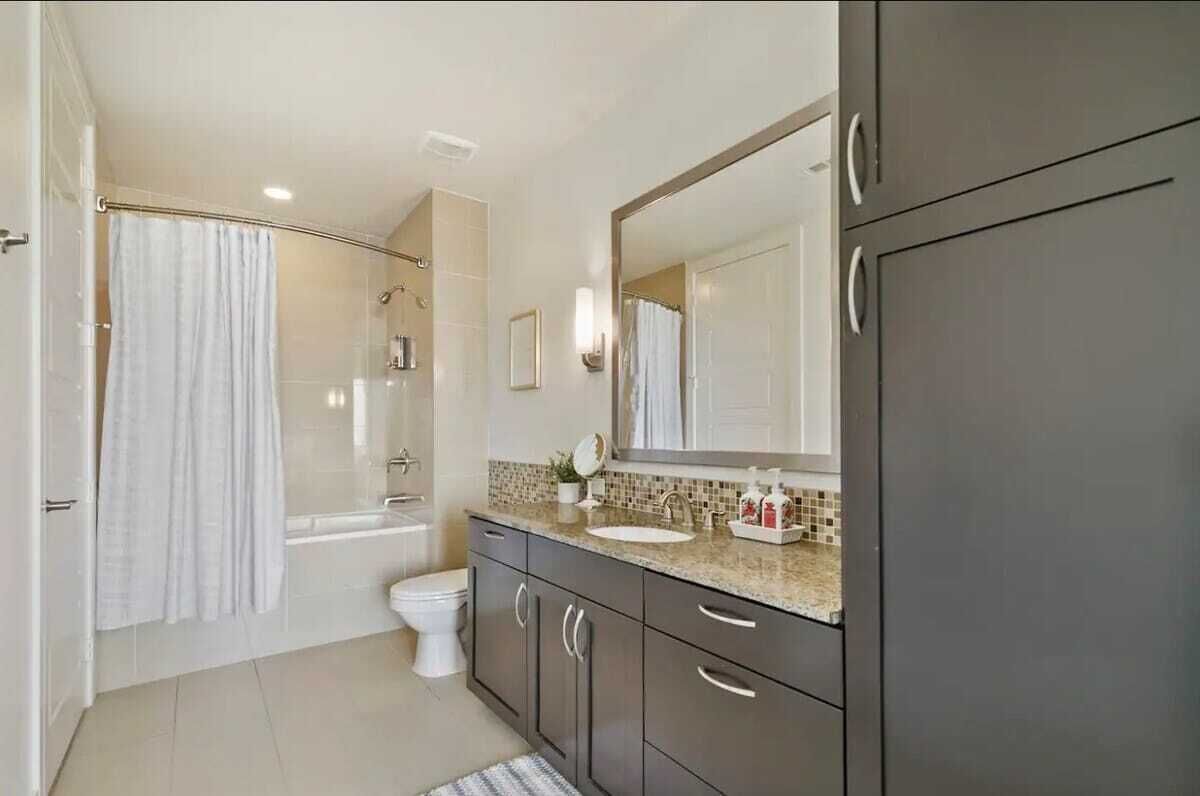 Un baño moderno con bañera, inodoro y tocador con un espejo grande.