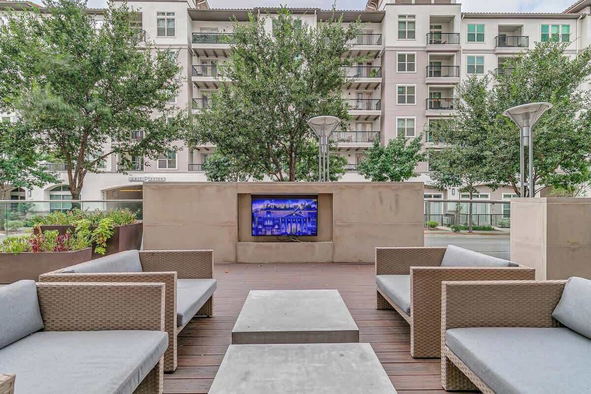 A rooftop terrace with outdoor seating, a flat-screen TV, and a view of a building with balconies.