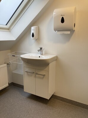 A modern bathroom with a skylight, a white sink, a towel dispenser, and a radiator.