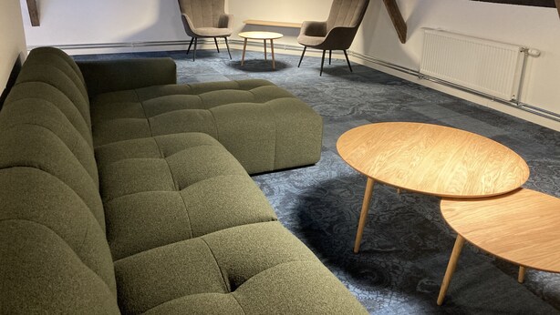En moderne loftlejlighed med en hjørnesofa, to runde træborde og to lænestole.