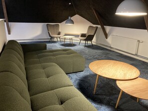 A modern loft with a sectional sofa, two round wooden tables, and two armchairs.