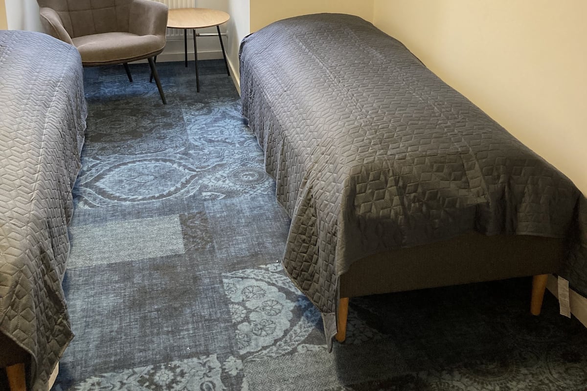 Ein Schlafzimmer mit zwei Einzelbetten, einem Sessel, einem kleinen Tisch und einem Fenster mit Jalousien.