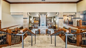 A spacious lobby with a central fountain, wooden railings, and a stone floor.