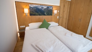 Un letto rifatto con lenzuola bianche e un cuscino verde, una testiera in legno con un dipinto di un paesaggio montano e armadi in legno con maniglie argentate.
