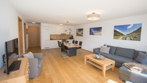 Un soggiorno moderno con un divano grigio, un tavolino in legno e una TV su un mobiletto in legno. Si nota anche un'area pranzo con tavolo e sedie, e una cucina sullo sfondo.