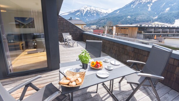 Un balcone con un tavolo apparecchiato per la colazione, un cesto di pane e una pianta in vaso.
