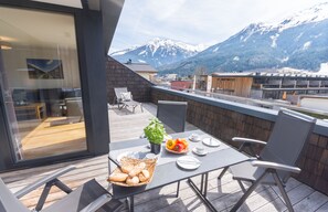 A balcony with a table set for breakfast, a basket of bread, and a potted plant. - Apartment am Sonnenhang - Top 3 (Neukirchen am Grossvenediger)