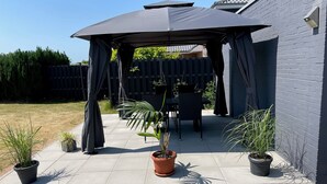 A patio area with a covered seating area, potted plants, and a fenced backyard.