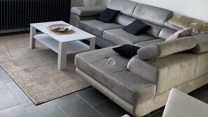 A modern living room with a grey sofa, a white coffee table, and a large window with blinds.