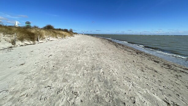 A sandy beach with a clear sky, a few people, and a lighthouse in the background.