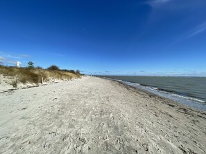 A sandy beach with a clear sky, a few people, and a lighthouse in the background.