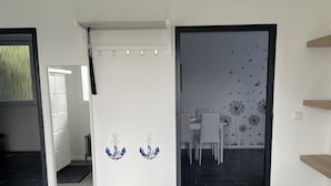 A modern interior with a tiled floor, a white wall with two blue anchors, a door leading to a dining area with a wall mural, and a small wooden shelf.