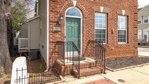 A brick building with a green door, a number '21321' sign, and a small porch with a white railing. - Prime Downtown Cornelius Townhome (Cornelius)