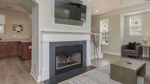 A living room with a fireplace, a television mounted above it, a sofa, and a coffee table. - Prime Downtown Cornelius Townhome (Cornelius)